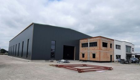 Ein im Bau befindliches Gebäude mit einem großen Garagentor, umgeben von Baustellenmaterialien und Gerüsten.