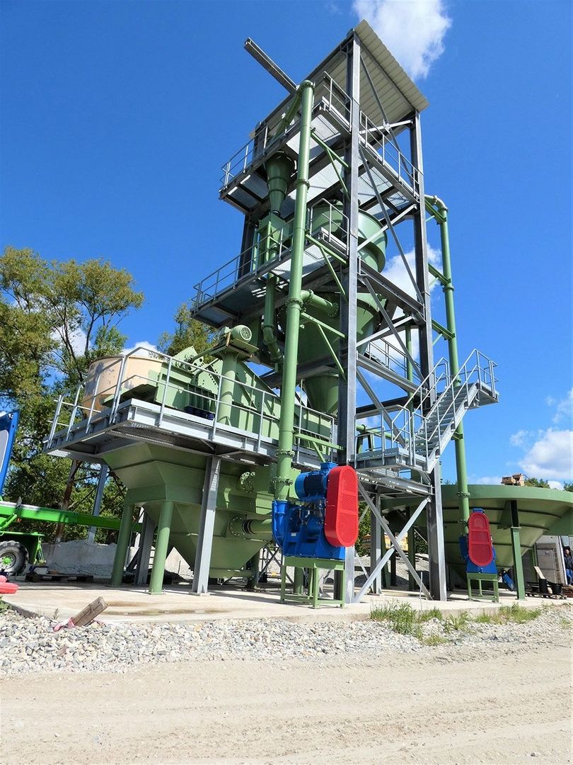 Zementwerk mit hohem Turm und Kran, umgeben von Industrieanlagen und Baustellenmaterialien.